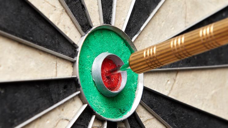 Pfeil steckt im roten Zentrum einer Dartscheibe mit schwarzen und weißen Feldern. Nahaufnahme der Zielscheibe.