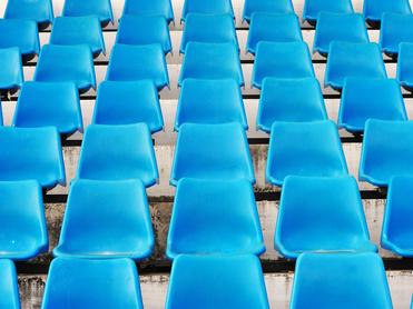 Reihe blauer Kunststoffstühle auf einer Tribüne, gleichmäßig angeordnet mit Sicht auf die Sitzflächen.